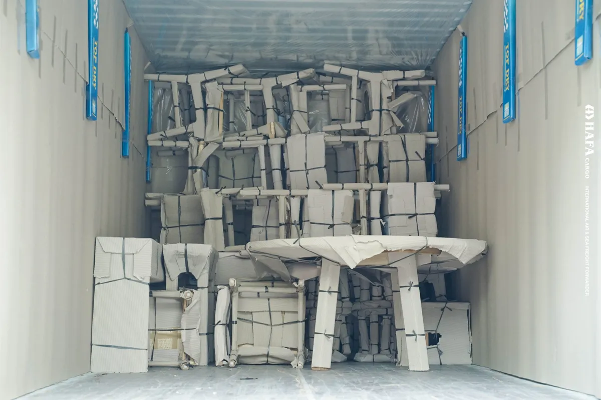 A shipping container packed floor to ceiling with wrapped and strapped furniture.
