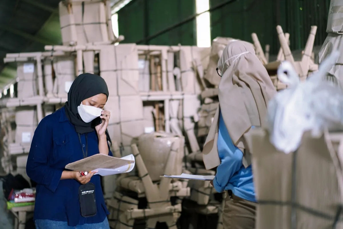 A HAFA Cargo staff member on the phone holding paperwork among stacked crates.
