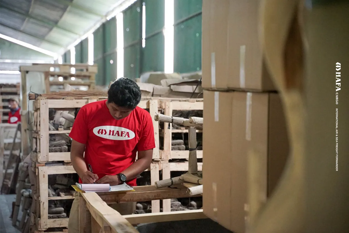 Un employé de HAFA Cargo contrôle une caisse en bois emballée, documents en main.