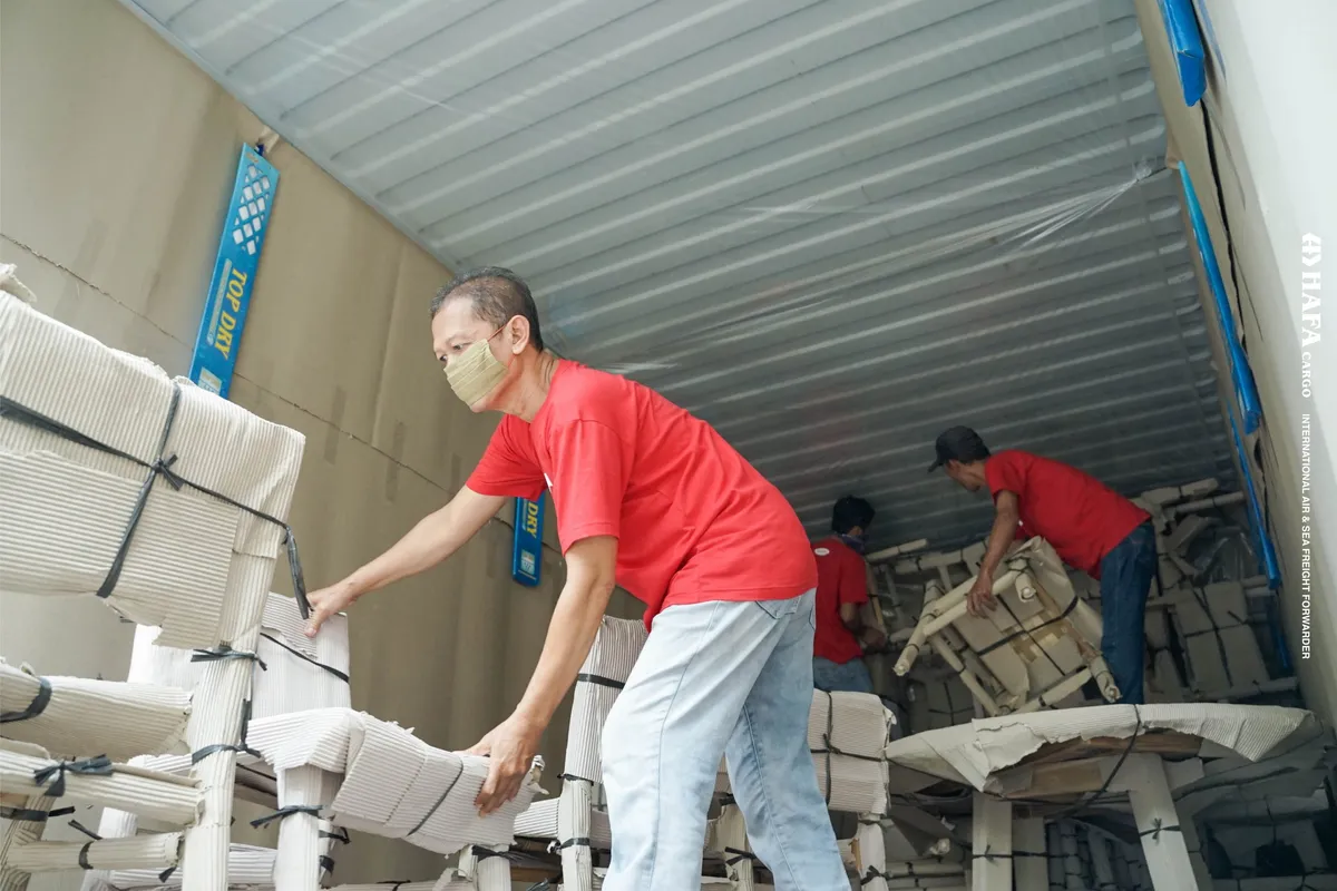 HAFA Cargo crew passing foam-wrapped furniture into a shipping container.