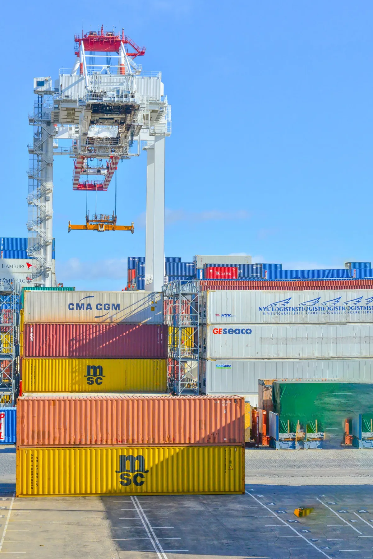Shipping containers stacked in a port yard with a crane behind.